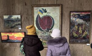 Сучасний український художник працює над картиною у майстерні, на полотні абстрактний пейзаж із яскравими кольорами та динамічними мазками.