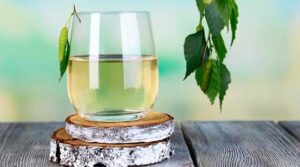 Склянка березового соку на дерев’яному тлі поруч з листком берези — натуральний напій весни