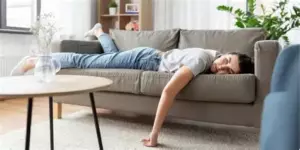 Людина сидить схилившись, притиснувши голову до колін, на тлі приглушеного освітлення — образ апатії і внутрішньої втрати енергії.