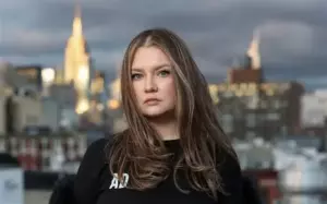 Анна Делві сидить у кав’ярні в елегантному пальто і сонцезахисних окулярах — характерний образ аферистки світського життя